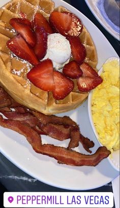 a plate with waffles, strawberries and bacon on it next to scrambled eggs