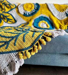 a yellow and blue crocheted blanket sitting on top of a gray couch next to a wooden floor