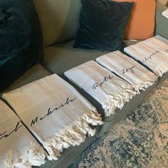 three pieces of cloth with writing on them sitting on a couch next to two pillows