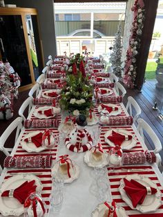 a table set for christmas dinner with red and white napkins, plates, silverware and flowers