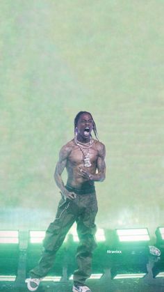 a man with no shirt on standing in front of a green bench and wearing white sneakers