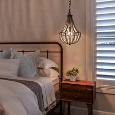 a bed with white sheets and pillows in a bedroom next to a window covered by blinds