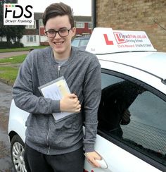 a young man standing next to a white car holding a binder in his hand