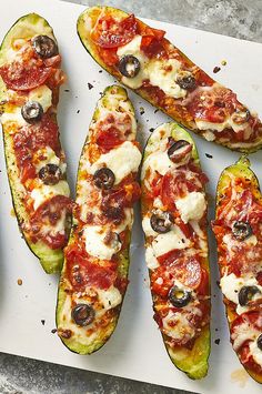 several slices of zucchini sitting on top of a cutting board with cheese and olives