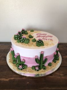 a birthday cake decorated with pink and white frosting, cacti and flowers