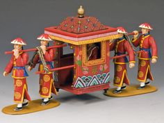 three figurines are standing in front of a red cart with gold trimmings