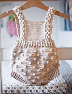 a crocheted baby bodysuit hanging on a wooden hanger in front of a bed