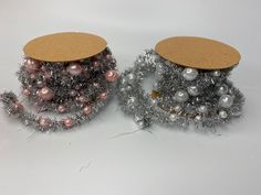 two silver and pink christmas decorations on white table with brown cardboard tag hanging from the top