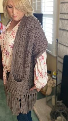 a woman standing in a room wearing a brown knitted shawl with fringes