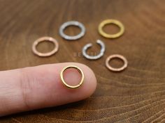 five different sized rings sitting on top of a wooden table next to someone's finger