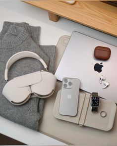 an apple laptop, headphones and other items on a table with a sweater in the background