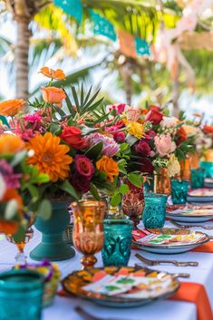 a long table is set with colorful flowers and place settings for an outdoor dinner party