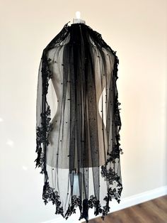 a sheer black scarf hanging on a wall next to a wooden floor and white walls