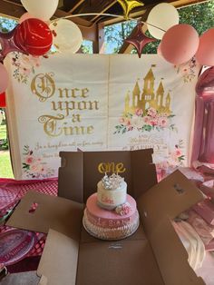 a cake in a box on top of a table at a birthday party with balloons