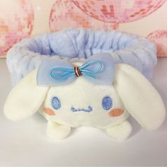 a white stuffed animal with a blue bow on it's head sitting next to a pillow