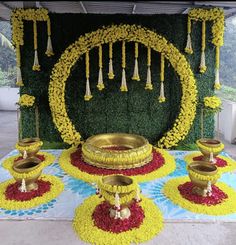 an arrangement of yellow and red flowers on display in front of a green wall with hanging candles