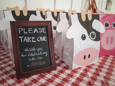 some paper bags are on a table with a cow sign and a chalkboard that says please take one thank you for celebrating with me