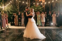 the bride and groom are sharing their first dance as guests look on in the background