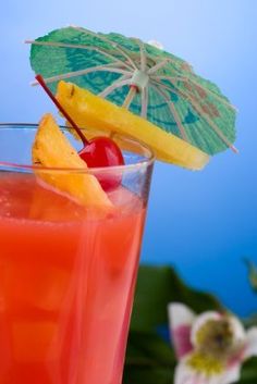 a drink with an umbrella and fruit on the top is sitting in front of some flowers