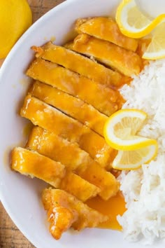 a white plate topped with chicken and rice next to lemons on top of a wooden table