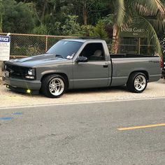 a gray truck parked in front of a fenced off area with palm trees behind it