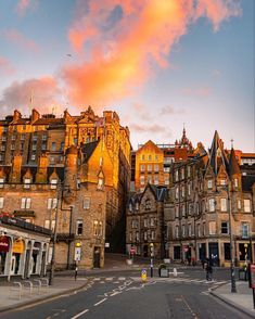 the sun is setting over old buildings in edinburgh, scotland as people walk down the street