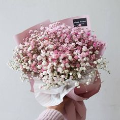 a person holding a bouquet of pink and white flowers in their hand with a card attached to it