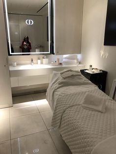 a white bed sitting in a bedroom next to a mirror and counter top with towels on it