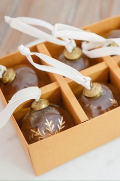 four chocolate covered ornaments in a box with white ribbon on the top and bottom, sitting on a table