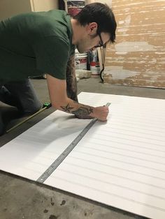 a man working on a large piece of paper with scissors and tape around his neck