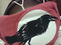 a black bird painted on the side of a red bag with white and black trim