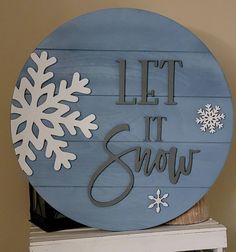 a wooden sign that says let it snow on top of a white shelf in front of a tan wall