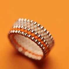 an orange and white beaded ring sitting on top of a yellow surface with two rows of beads