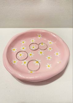 a pink plate with three rings on it and daisies painted on the side, sitting on a white surface