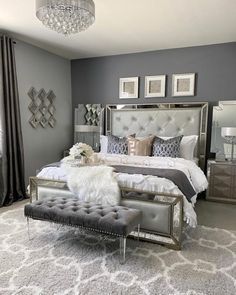 a bedroom decorated in gray and silver with a large bed, chandelier, pillows, rugs, and pictures on the wall