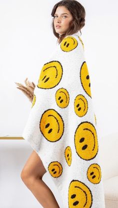 a woman standing in front of a white wall with yellow smiley face ponchles on it