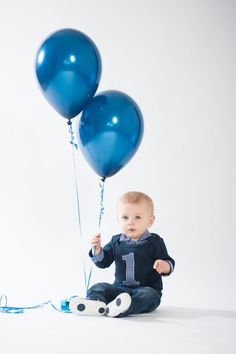 a baby sitting on the ground holding two blue balloons