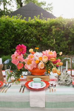 a table set with plates, silverware and flowers in an orange vase on it