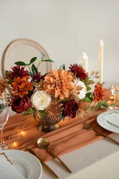 a vase filled with flowers sitting on top of a table next to plates and candles