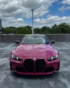 the front end of a pink sports car parked in a parking lot with clouds overhead