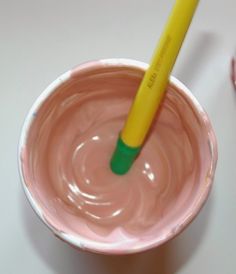 a yellow and green toothbrush sticking out of a pink cup filled with melted chocolate