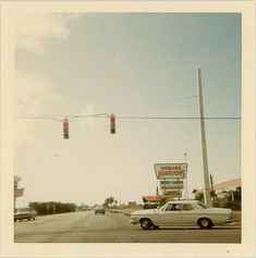 an old photo of a car driving down the road in front of a gas station