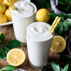 two glasses filled with lemonade sitting on top of a table next to sliced lemons