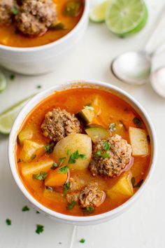 two bowls filled with meat and vegetable soup on top of a white table next to spoons