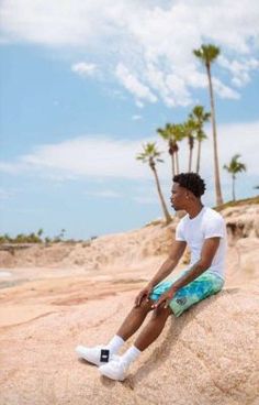 a man sitting on top of a sandy beach next to the ocean and palm trees