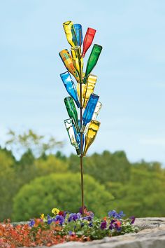 a multicolored glass wind chime on top of a rock in front of some flowers