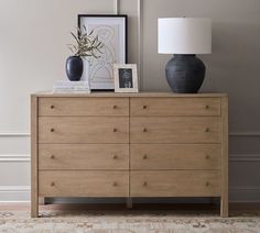 a wooden dresser with two vases on top of it and a lamp next to it