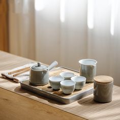 a tray with cups and spoons on top of a wooden table next to a window