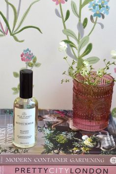 glass bottle midsummer room spray on gardening books next to small pink glass vase with white flower and floral wallpaper backdrop Container Gardening, Hand Poured, Glass Bottles