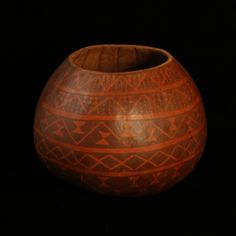 an orange vase sitting on top of a black table next to a wooden bowl with geometric designs